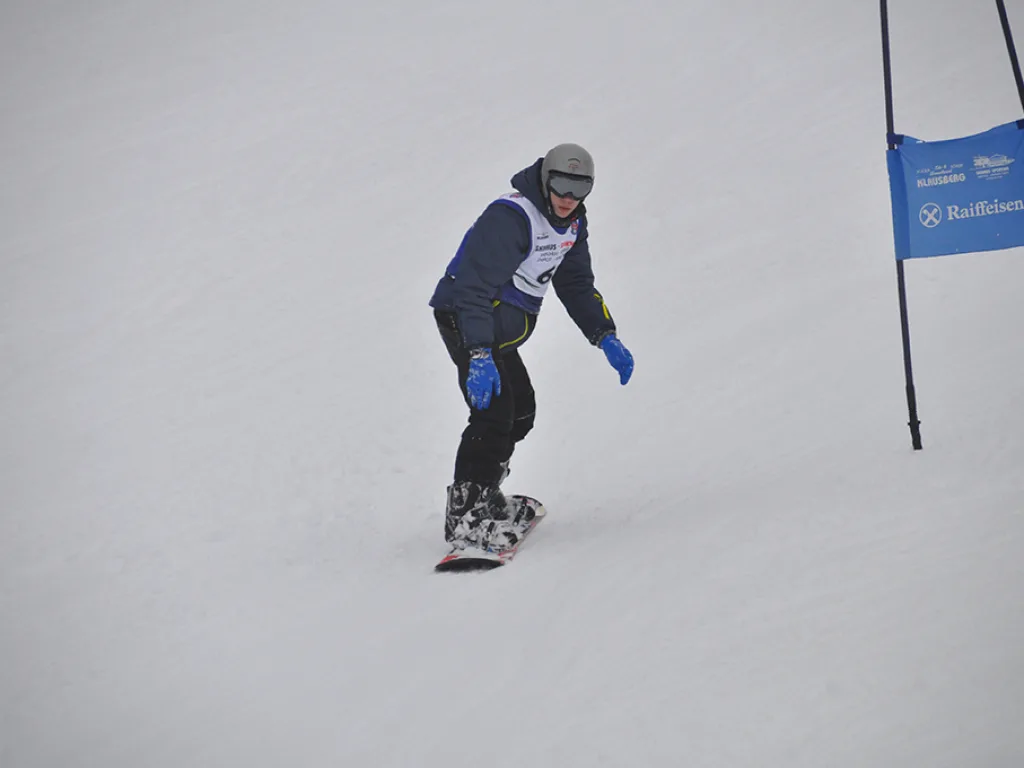 Snowboarder in grauer Jacke neben dem blauen Tor.